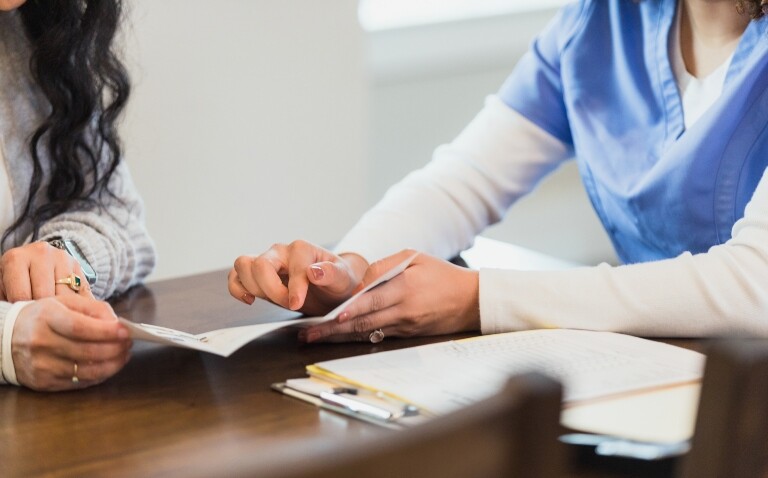 A close-up of a patient and a doctor in scrubs looking over a patient information leaflet to illustrate the finding that AI successfully simplifies complex interventional radiology information for patients