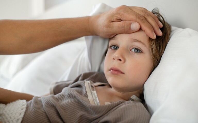 A young girl in bed with her parent's hand over her forehead to illustrate an antibiotic stewardship programme leading to a two-fold increase in optimal antibiotic use for pneumonia in children