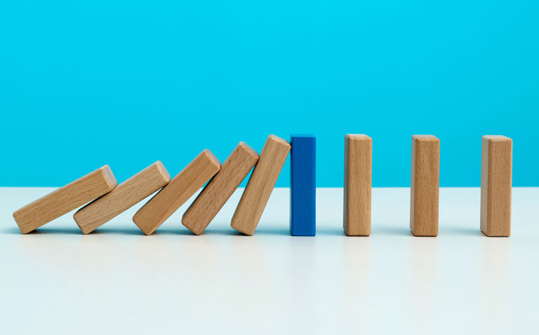 A row of wooden dominoes with five on the left hand side toppling over to meet a blue domino stood on its end and three more wooden dominos on the right to illustrate the role of clinicians in deprescribing and the DIAMOND programme