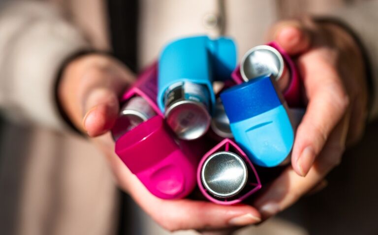 Close up of a woman's hands holding multiple blue and pink pressurised metred dose inhalers