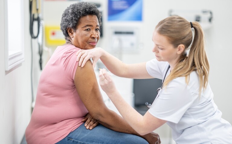 An older lady wearing a pink tshirt and jeans sitting in a medical setting with a healthcare professional wearing white scrubs administering a vaccination to illustrate the risk of Guillain-Barré in older adults after receiving the RSV vaccine
