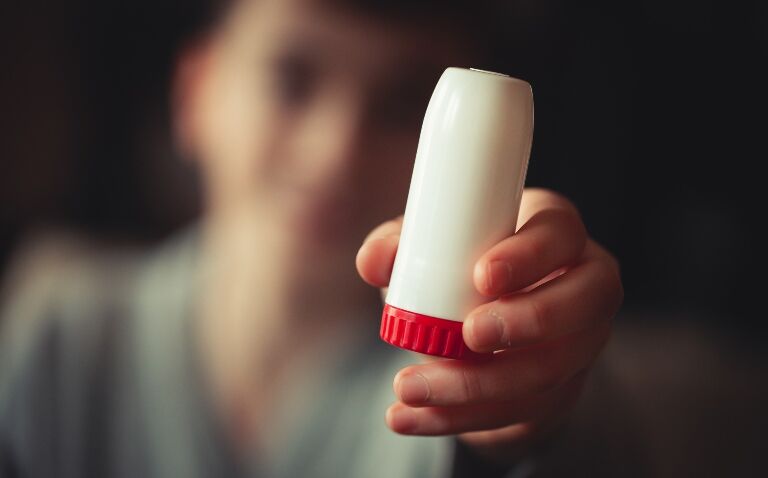 An out of focus man in the background holding a budesonide/formoterol inhaler to illustrate pharmacological management recommendations from the new chronic asthma joint guidelines