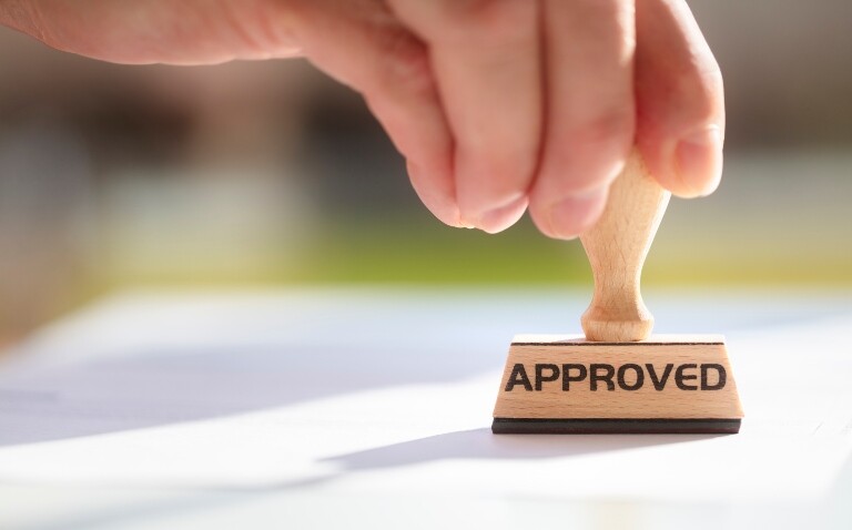 A wooden stamp with the word approved on it being stamped on a piece of paper to illustrate the MHRA approval of the twice-yearly biologic depemokimab for the treatment of severe eosinophilic asthma and severe chronic rhinosinusitis with nasal polyps