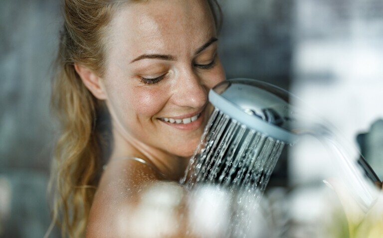 A close up of a smiling woman's head and shoulders while she is showering to illustrate the finding that eczema symptoms are unaffected by bathing frequency