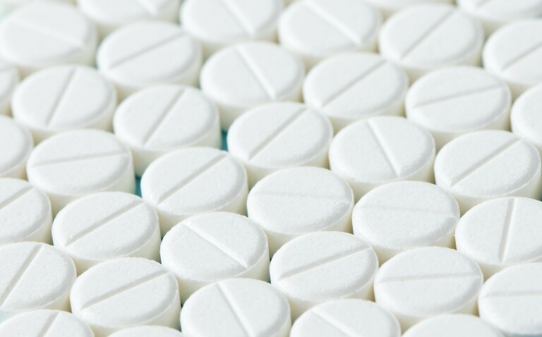 Close up of white round tablets with lines down the centre lined up to represent beta-blockers and illustrating the differing evidence of their use post myocardial infarction in patients with LVEF