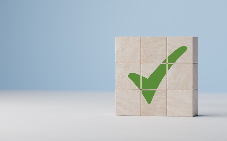 Nine wooden blocks stacked together with a green tick across them all on a white and blue background to illustrate the first needle-free anaphylaxis treatment being approved in the UK