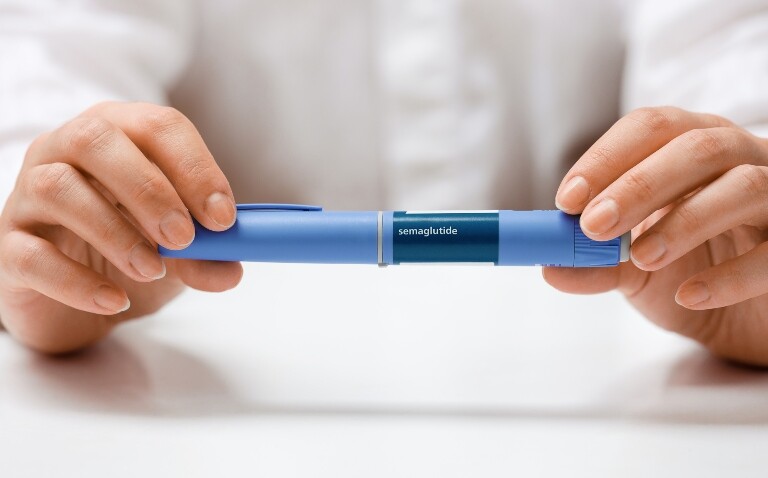 A woman sat at a table holding a semaglutide injector to illustrate the finding that GLP-1RAs have been found to have a protective effect in psoriasis