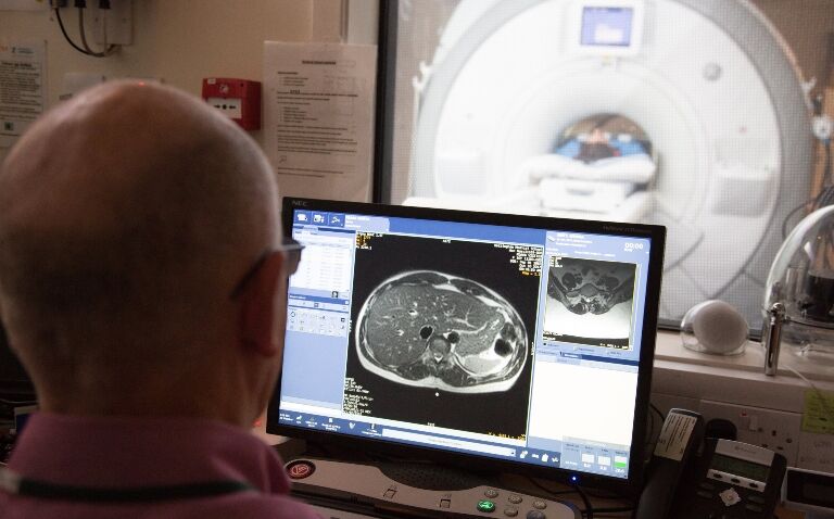 Dr Luca Marciani observing MRI results on a computer screen with an MRI scanner in the background to illustrate the results of novel research into gluten-free diets in coeliac disease