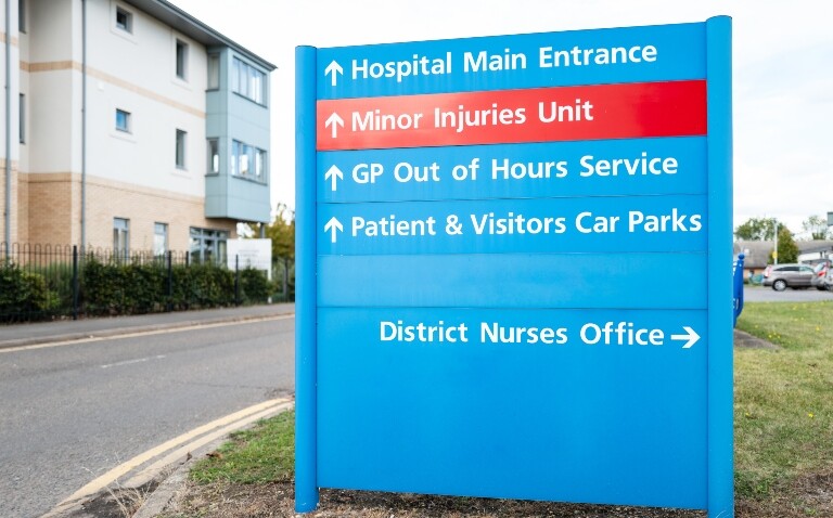 A blue sign outside a hospital building with direction arrows for services such as main hospital entrance