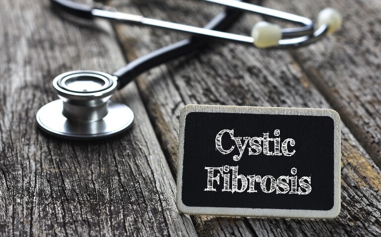 Cystic Fibrosis written on blackboard with a stethoscope behind it on wooden planks to illustrate a once-daily cystic fibrosis treatment being available on the NHS