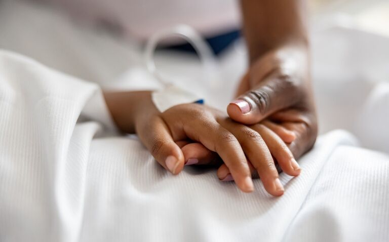 Close-up of a parent holding a child's hand with an catheter representing IV antibiotics and procalcitonin testing