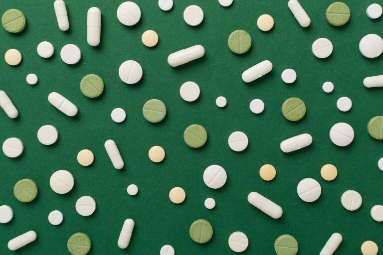 A selection of white, green and yellow capsules and tablets spread out on a dark green background to illustrate eco-directed sustainable prescribing practices