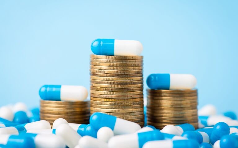 Three stacks of coins surrounded by blue and white capsules to represent sustainable and cost-effective drug use in hospitals