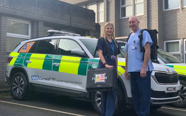 Two members of the NHS Cornwall and Isles of Scilly integrated care system X-ray car service standing in front of an NHS Cornwall 111 Integrates Urgent Care Services car and holding bags of the X-ray equipment