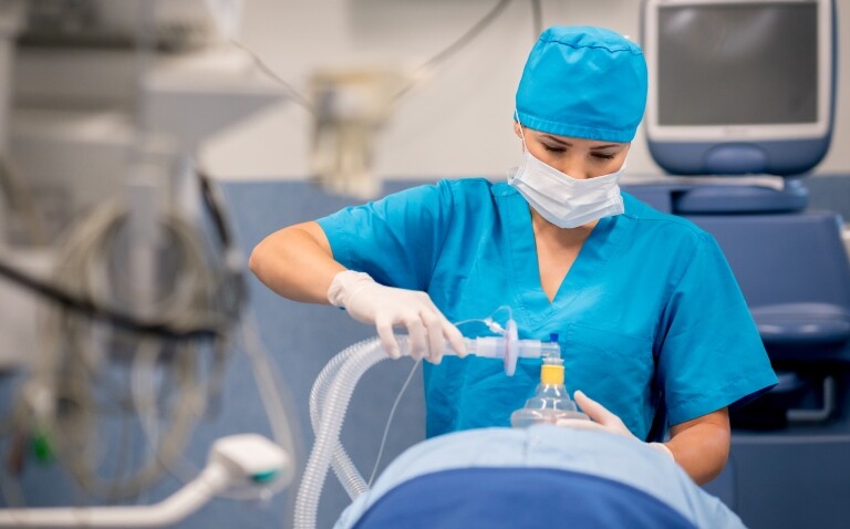 A female healthcare professional putting a mask on a patient in an operating theatre to demonstrate measures to reduce the emissions impact of anaesthetic gases such as desflurane on healthcare systems and improve their carbon footprint