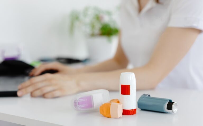 A healthcare professional sits at a desk typing on a computer with different types of inhalers in the foreground