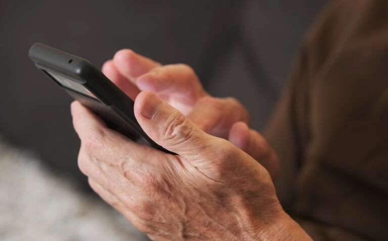 A close up of an old man holding a smartphone and looking at an eHealth app for abdominal aortic aneurysm care