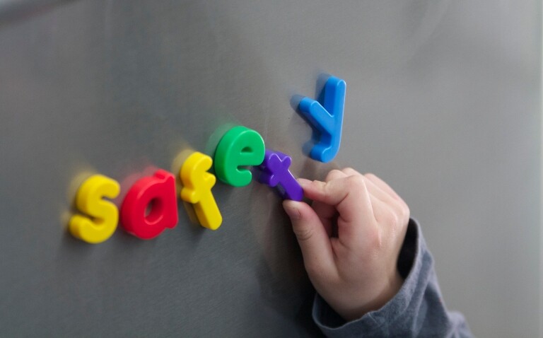 A close-up of a silver fridge with multicoloured letter magnets spelling out safety and a child's hand holding onto the letter T to illustrate a rise in magnet ingestion prompting urgent calls to action