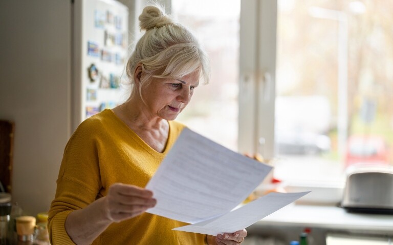 An older woman in a yellow jumper reading a letter in a kitchen by a window to represent timed appointments being superior to open invitations for lung cancer screening