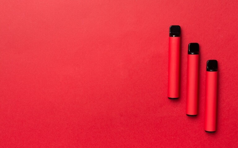 Three red single-use vapes on a red background to illustrate the UK's single-use vape ban coming into effect
