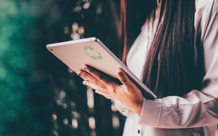 Woman holding a tablet computer with a green recycle symbol on the back to illustrate the launch of Hospital Healthcare Europe's new sustainability zone