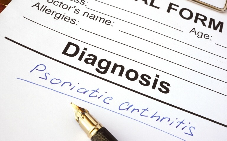 A diagnosis form with the words psoriatic arthritis written in blue pen and a fountain pen laying across it to illustrate the discovery that TNF-alpha inhibitors reduce the incidence of PsA in patients with severe psoriasis