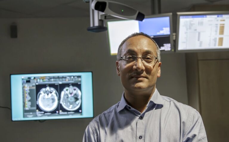Professor Raj Jena standing in front of screens showing medical images to illustrate the transformative use of AI in radiotherapy