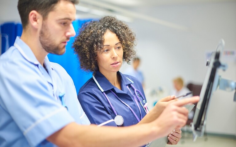 Male and female nurses reviewing patient data on a touchscreen monitor in a hospital to illustrate RCEM strategies to improve time critical medication (TCM) identification and administration