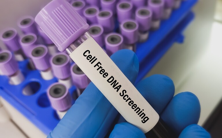 A blue-gloved hand holding a test tube of blood with a Cell Free DNA Sampling label on it for paediatric cancers and a test tube rack in the background
