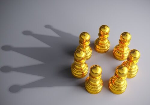 Seven gold coloured chess pawns in a circle making a shadow of a crown on a grey background to represent gold-standard MDT support in breast cancer care with support from Breast Cancer Now