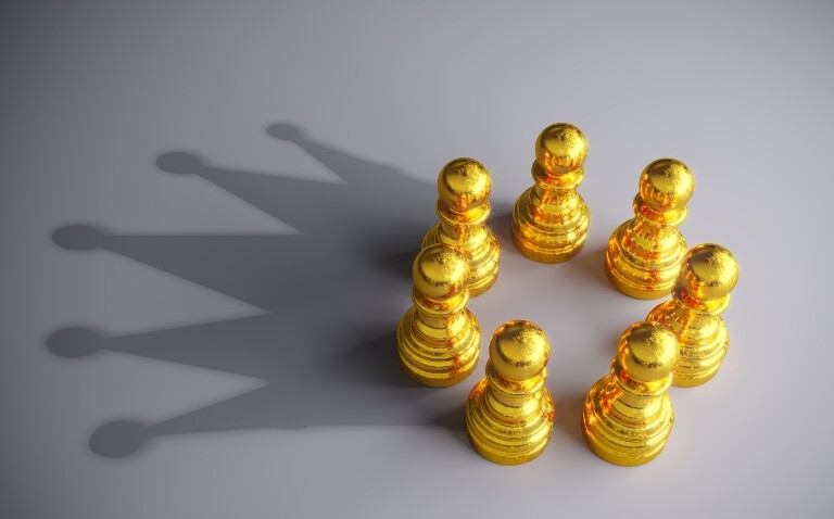 Seven gold coloured chess pawns in a circle making a shadow of a crown on a grey background to represent gold-standard MDT support in breast cancer care with support from Breast Cancer Now
