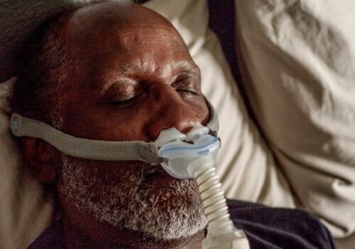 A close-up of an older gentleman asleep in bed wearing a CPAP machine to illustrate a new ERS consensus statement on the use of advanced telemedicine in obstructive sleep apnoea