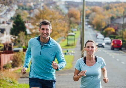 A man and a woman running on a path with a residential neighbourhood in the background to illustrate air pollution significantly weakening the health benefits of exercise