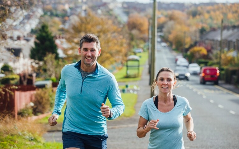 A man and a woman running on a path with a residential neighbourhood in the background to illustrate air pollution significantly weakening the health benefits of exercise