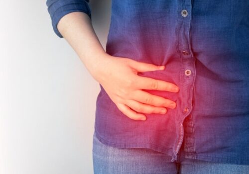 A close up of a woman holding her right hand side with a glowing red circle over the top of her hand to illustrate 10-year data showing antibiotics as viable for uncomplicated acute appendicitis in adults