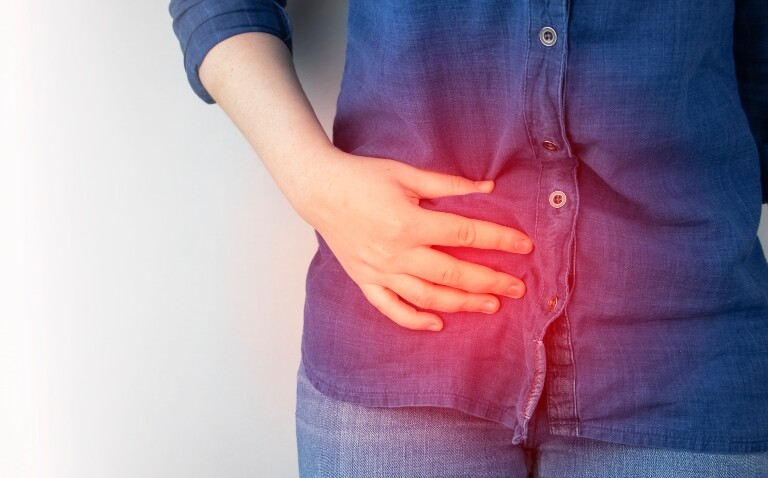 A close up of a woman holding her right hand side with a glowing red circle over the top of her hand to illustrate 10-year data showing antibiotics as viable for uncomplicated acute appendicitis in adults