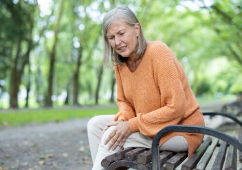 Senior woman feeling knee pain sitting on bench in park