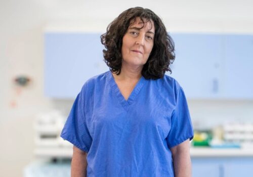A headshot of Professor Felicity Meyer standing in a hospital in blue scrubs to illustrate women in surgery