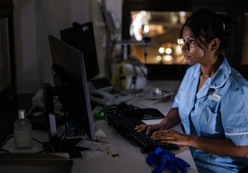 A nurse sitting at a desk and working on a computer in the dark to illustrate a night shift