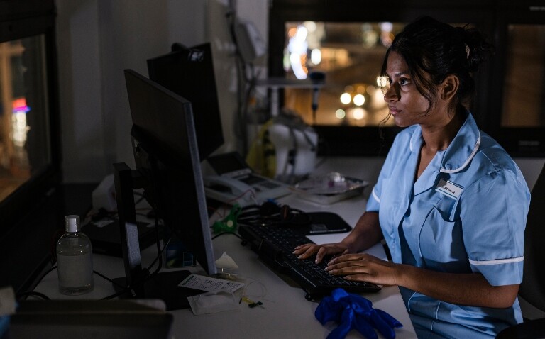 A nurse sitting at a desk and working on a computer in the dark to illustrate a night shift