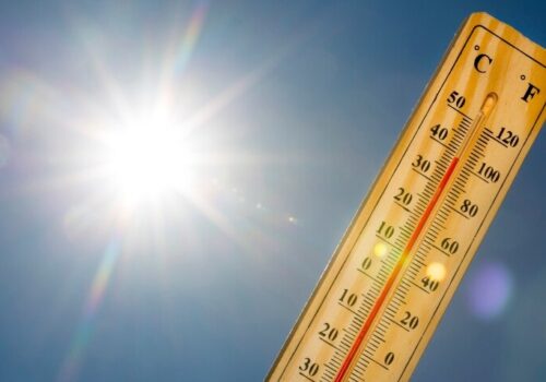 A mercury thermometer marking 39 degrees Celsius 100 Fahrenheit against a blue sky with blazing sun