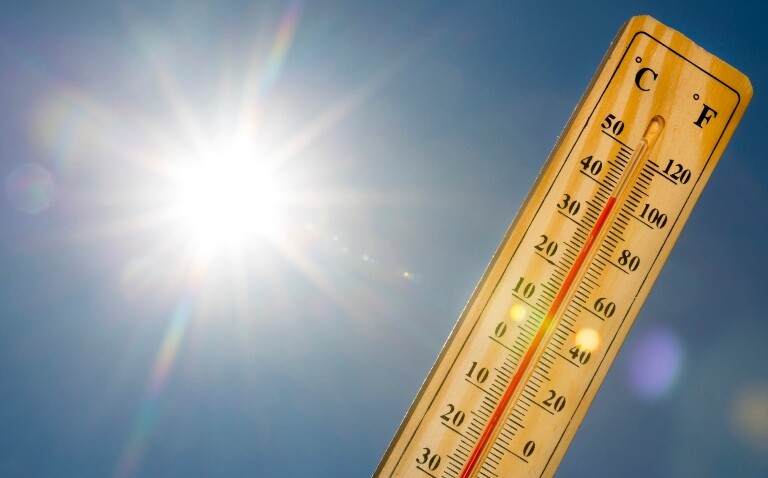 A mercury thermometer marking 39 degrees Celsius 100 Fahrenheit against a blue sky with blazing sun
