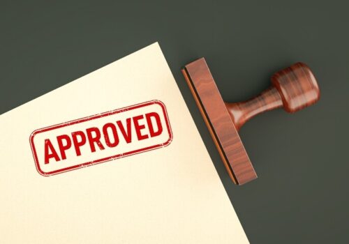 An approved stamp on the corner of a piece of paper with a wooden stamp laying next to it to illustrate deuruxolitinib being approved by the MHRA for severe alopecia areata