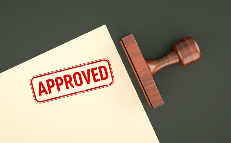 An approved stamp on the corner of a piece of paper with a wooden stamp laying next to it to illustrate deuruxolitinib being approved by the MHRA for severe alopecia areata