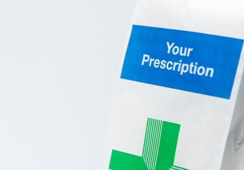 A close up of a white prescription bag with a pharmacy green cross on it and the words Your Prescription in a blue box above it to illustrate that discharge-focused audit and feedback by antibiotic stewardship teams fail to reduce antibiotic overuse