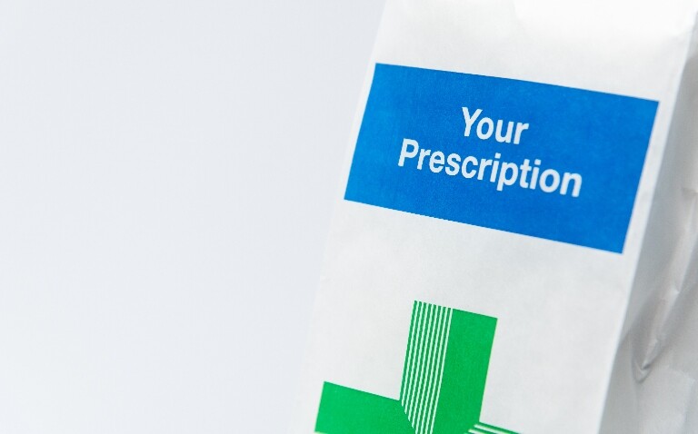 A close up of a white prescription bag with a pharmacy green cross on it and the words Your Prescription in a blue box above it to illustrate that discharge-focused audit and feedback by antibiotic stewardship teams fail to reduce antibiotic overuse