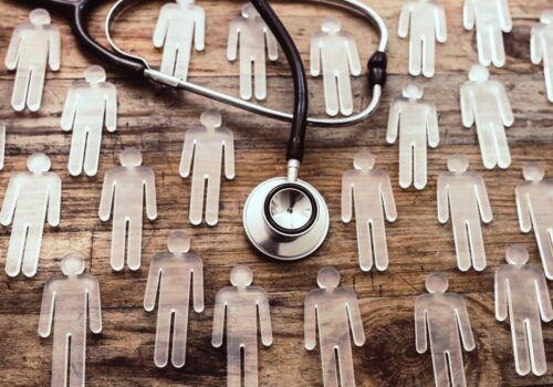 Stethoscope placed on a wooden surface surrounded by transparent human-shaped figures, symbolising healthcare, patient populations or clinical research