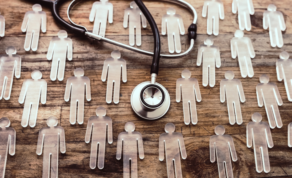 Stethoscope placed on a wooden surface surrounded by transparent human-shaped figures, symbolising healthcare, patient populations or clinical research