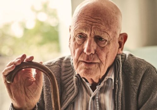 A close up of an elderly man sititng in his house with a walking stick to illustrate the finding that frailty affects outcomes after myocardial infarction differently in men and women