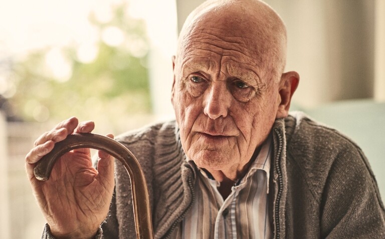 A close up of an elderly man sititng in his house with a walking stick to illustrate the finding that frailty affects outcomes after myocardial infarction differently in men and women